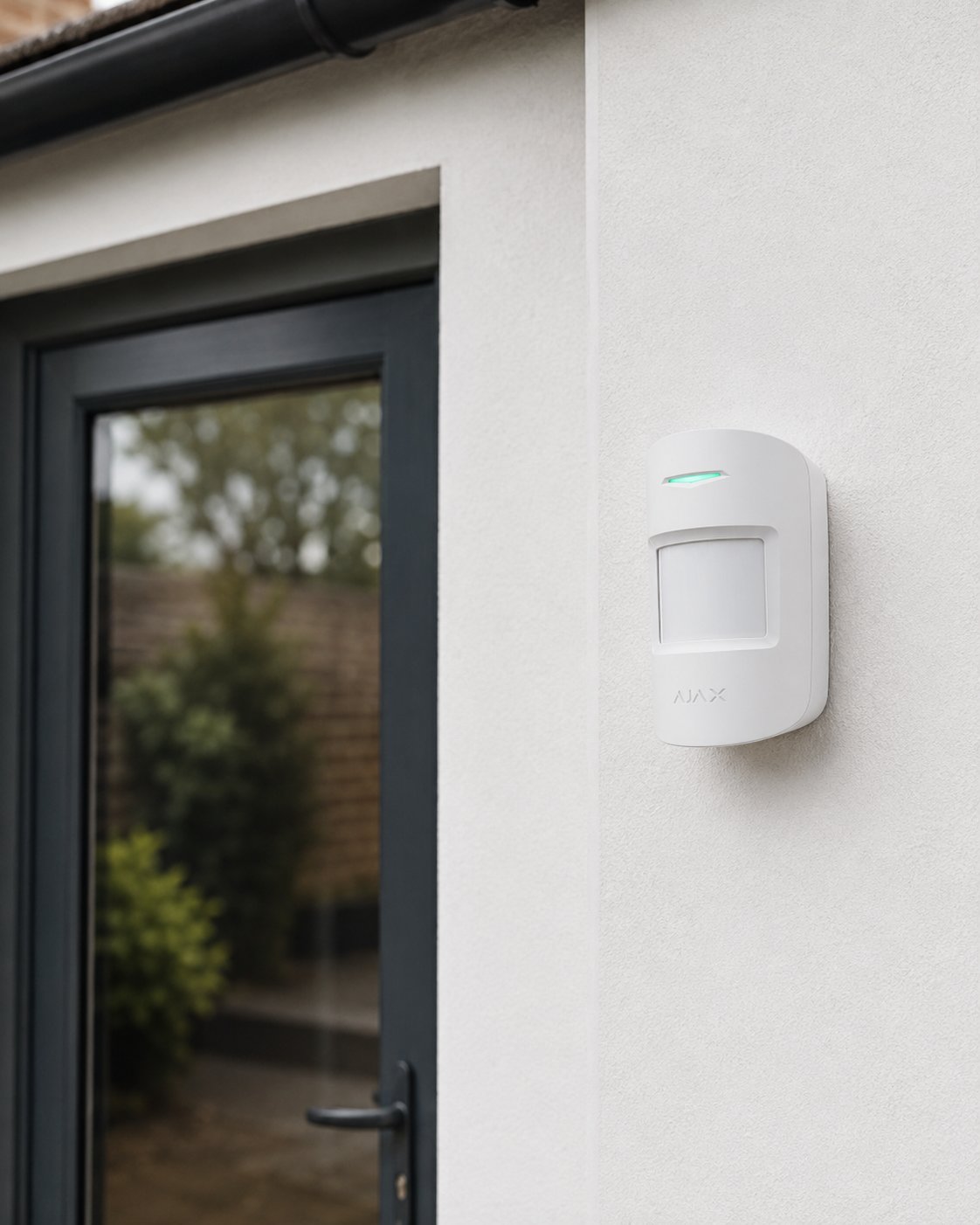 Ajax wireless motion sensor mounted on an exterior wall next to a glass door